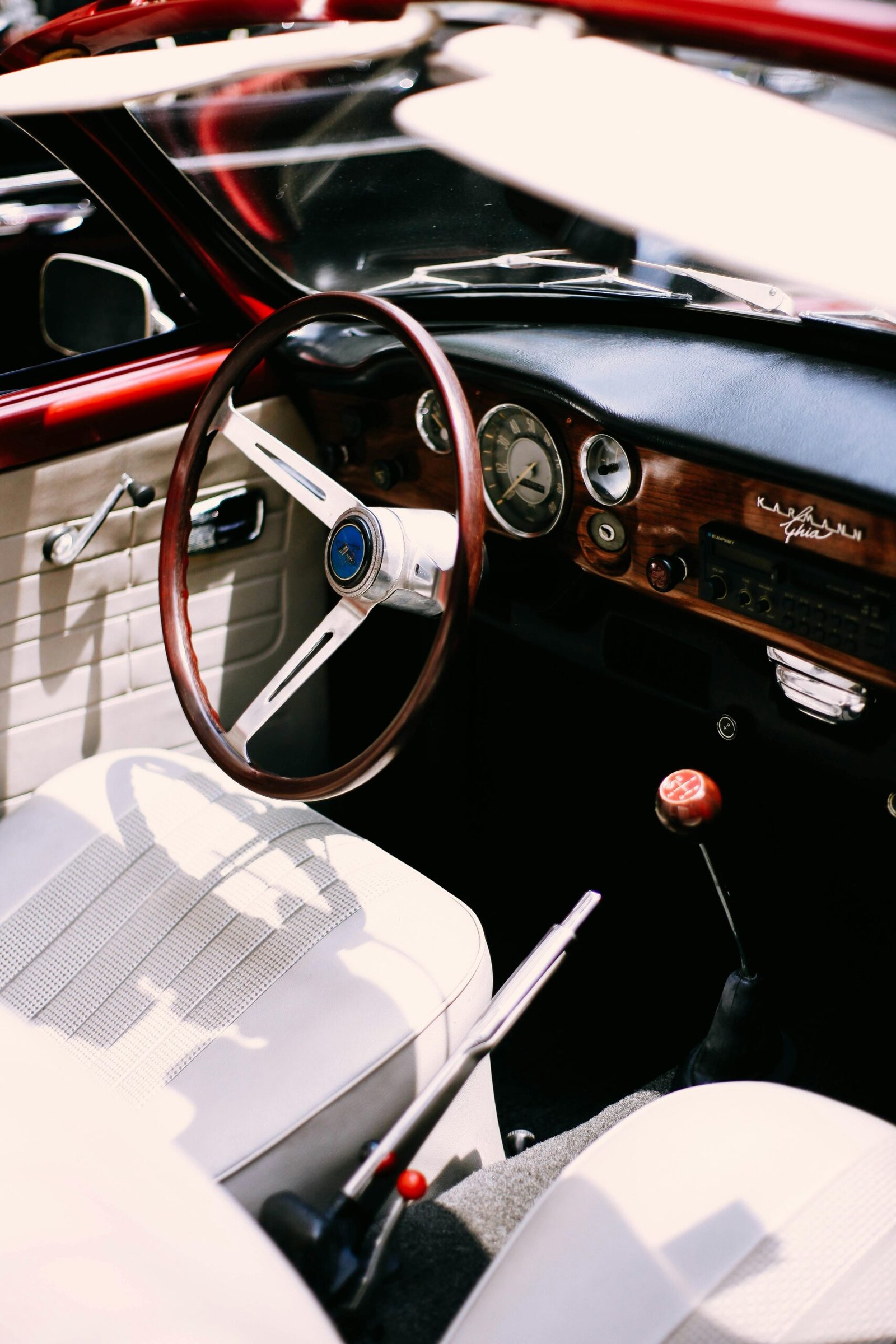 A vintage car interior featuring a wooden dashboard, steering wheel, and beige leather seats.